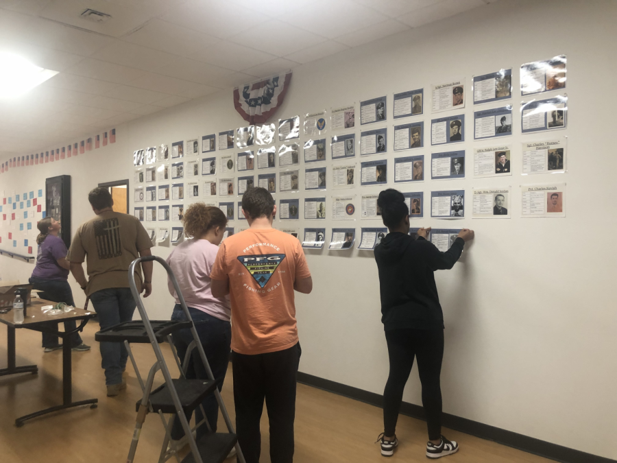 History club students assist adviser Marj DeNeal in hanging the individual photos that comprise the World War 1 and 2 Memorial currently on display in the history wing. 