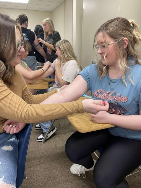 Freshman Eden Douglas and sophomore Kylee Bridewell apply tourniquets to freshman Mackenzie Reeves and Madalyn Poores arm before practicing injections at Allied Health Day.